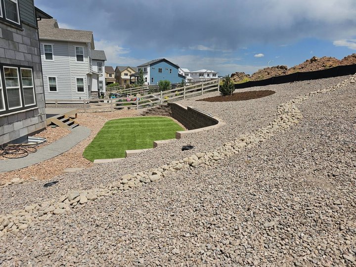 Block retaining wall with a rock dry-creek drainage channel carrying water away from the slope