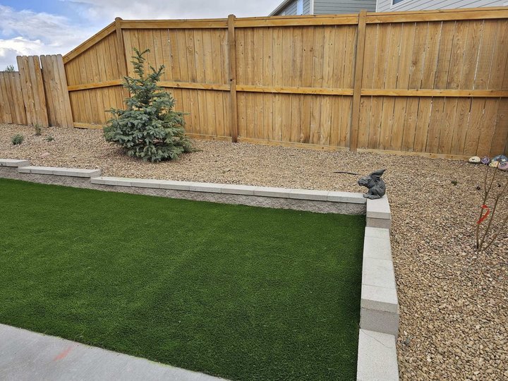 Block retaining wall built on proper base prep next to an artificial turf lawn
